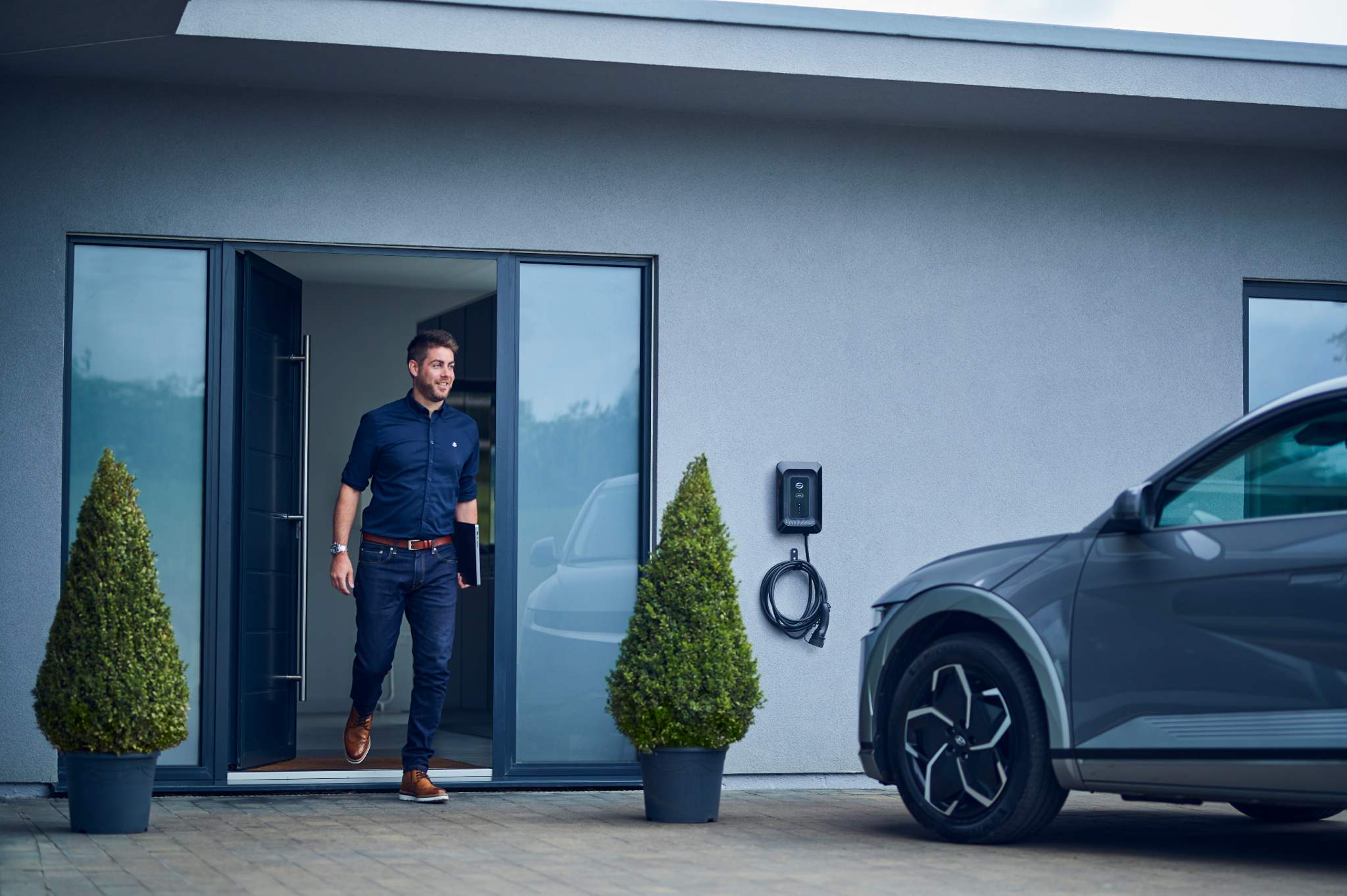 Casually dressed man existing modern house heading to to Electric Vehicle