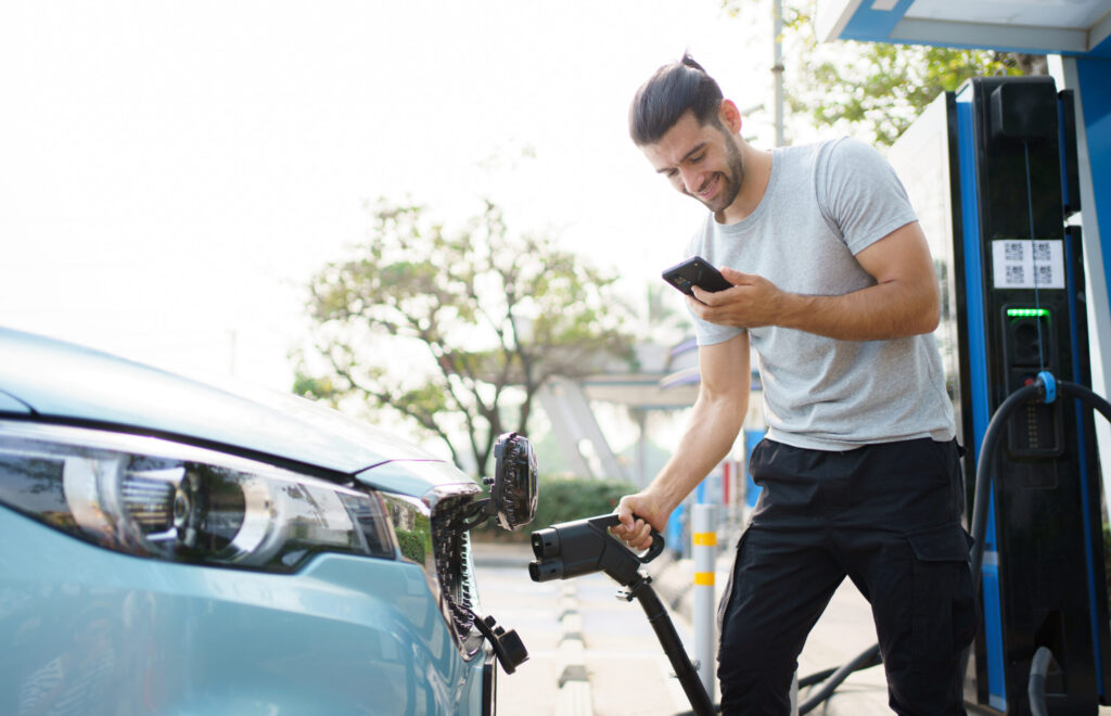 A young man holding an EV plug attaches the car to the charger