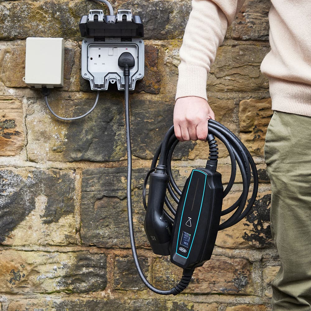 Man holding a 3-pin 'granny charger' EV cable plugged into the wall