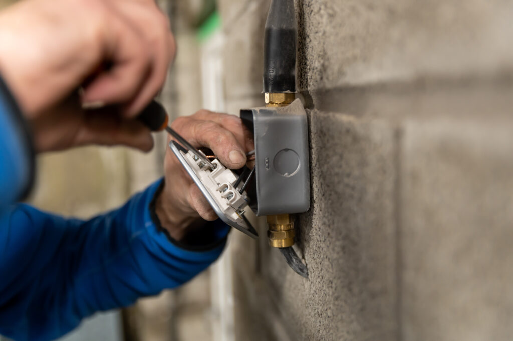An electrician is screwing in wiring in a socket on a wall