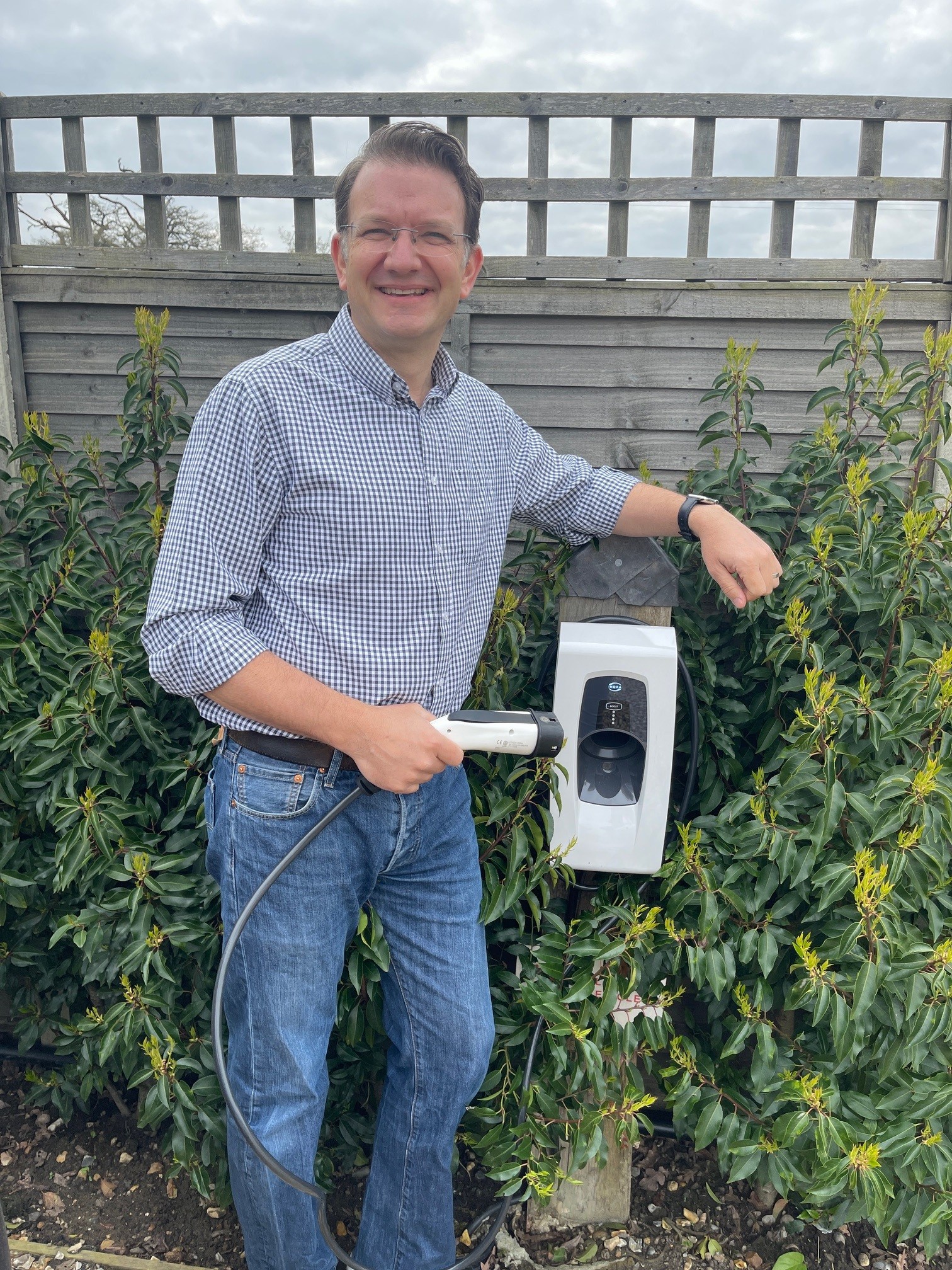 Man holding a smart charger plug in front of a fence and a mounted Indra Smart PRO