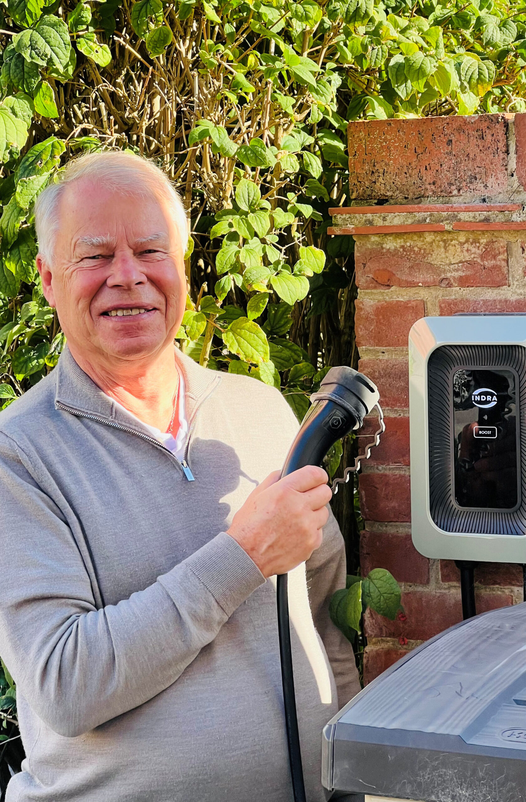 Man holding charging cable plug in front of an Indra Smart LUX charger