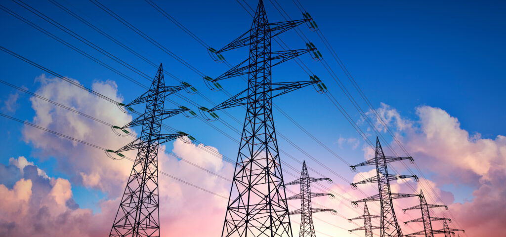 Power lines held by giant pylons with blue and cloudy sky behind