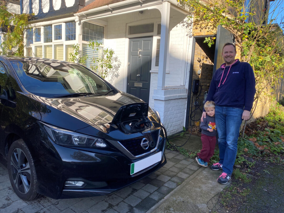 Man and his son standing beside a home charging EV outside a house.