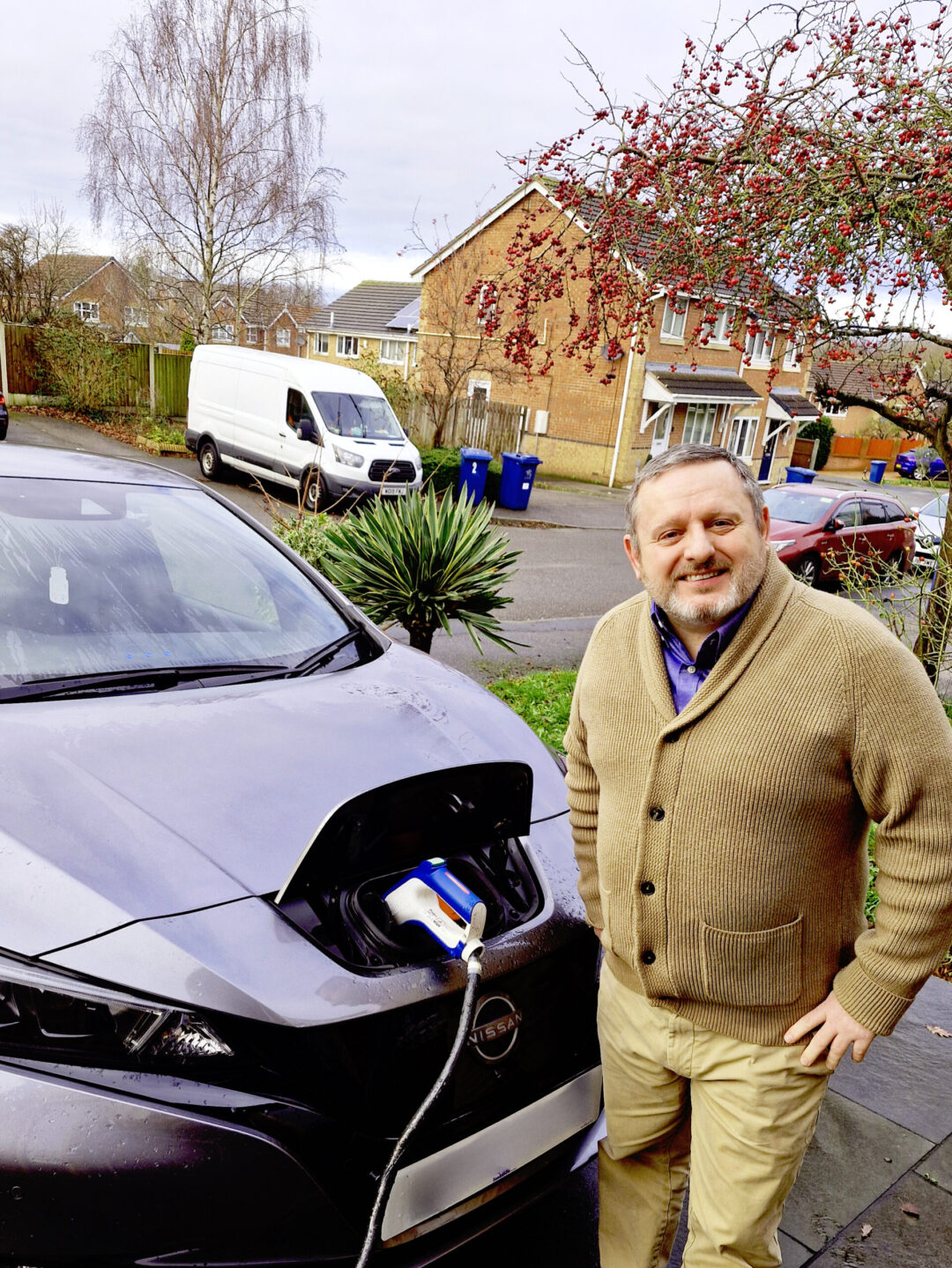 Smiling man standing beside a plugged in and charging EV 