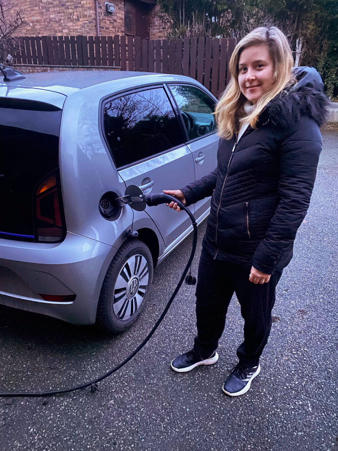 A woman holding a charging cable beside a small grey EV