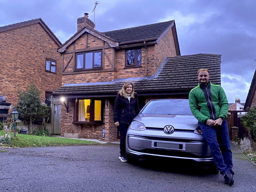 A couple standing by a small grey VW Up outside a house